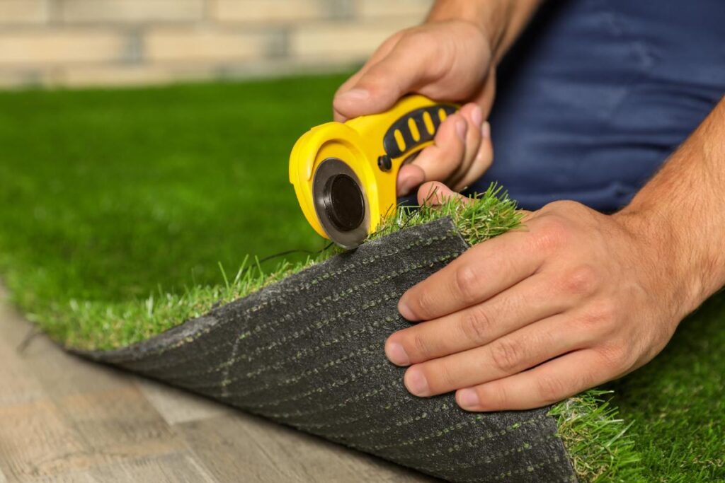 Une personne qui réalise une pose de gazon synthétique dans un jardin