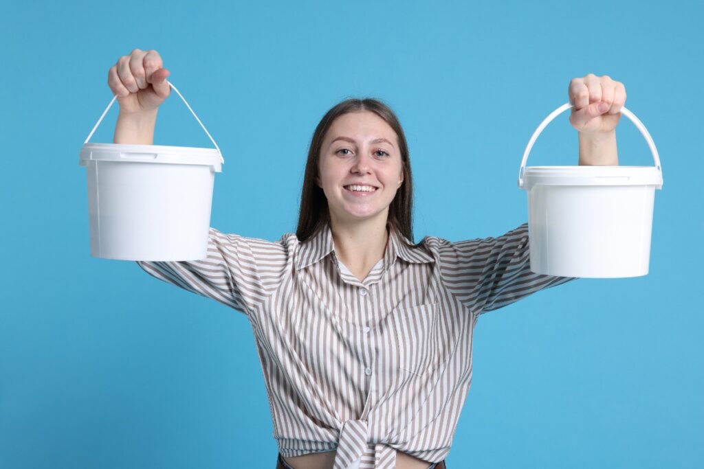 Une femme souriante tenant deux seaux blancs