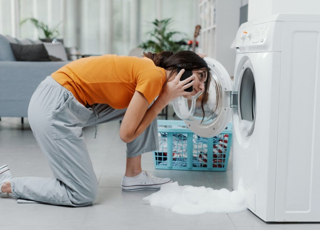 Une femme au téléphone et agenouillée devant la machine à laver