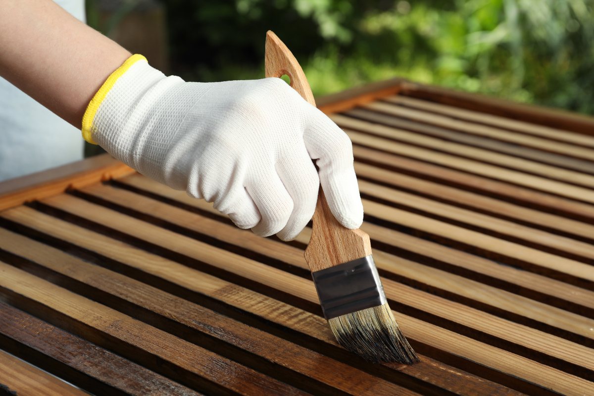 Main gantée appliquant de la teinture sur une surface en bois